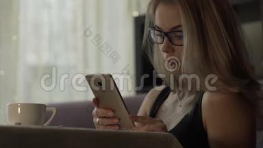 戴眼镜的年轻女子用手机端着咖啡杯站在桌旁